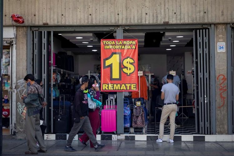 Fotografía de archivo fechada el 13 de enero de 2021, que muestra a personas mientras caminan frente a un cartel donde se lee "toda la ropa importada a un dólar", en Caracas (Venezuela). EFE/Rayner Peña R.