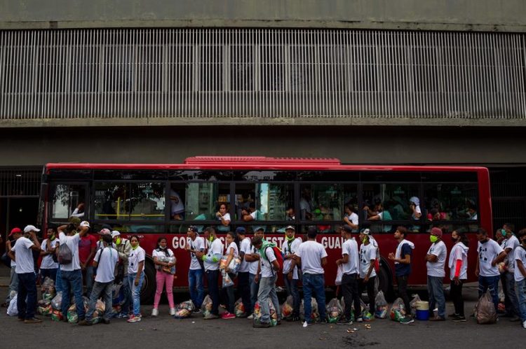 Un grupo de personas con bolsas de comida hace fila para montarse en un bus al finalizar un concierto para pedir la libertad del empresario colombiano Álex Saab, presunto testaferro del presidente de Venezuela, Nicolás Maduro,  en Caracas (Venezuela). EFE/