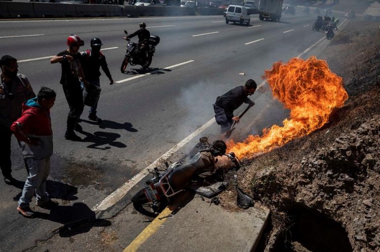 Un paramédico intenta apagar una motocicleta incendiada en una autopista el 2 de febrero de 2021, en Caracas (Venezuela). EFE/ Rayner Peña R