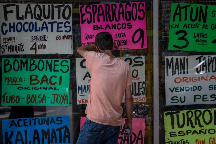 Un hombre observa dentro de una vitrina de la que cuelan carteles con precios de alimentos en Caracas (Venezuela). EFE/ Miguel Gutiérrez/Archivo