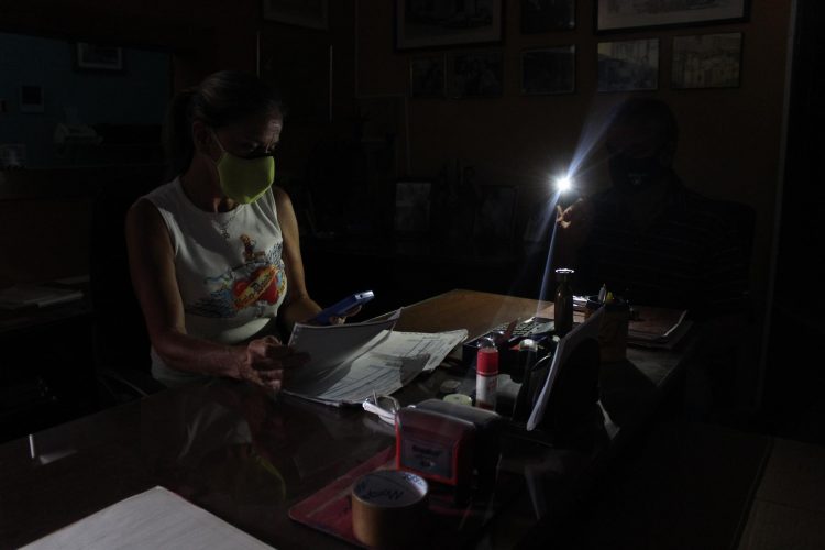 Una mujer revisa facturas mientras un hombre le ayuda a iluminar con un teléfono celular dentro de un local comercial en San Cristóbal (Venezuela). EFE