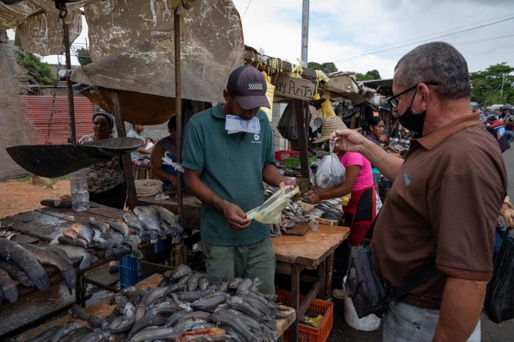 Un vendedor de alimentos fue registrado al sostener billetes en su boca, mientras despacha una venta de pescado, en el mercado municipal de San Félix (estado venezolano de Bolívar). EFE/Rayner Peña