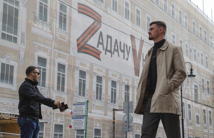 Dos hombres caminan este miércoles cerca de una gran pancarta que dice "La tarea será ejecutada" y colocada en la fachada de un edificio en el centro de Moscú. EFE/EPA/MAXIM SHIPENKOV
