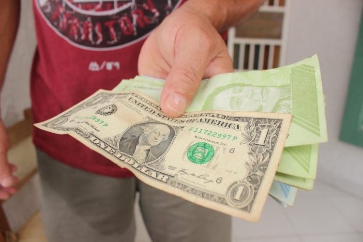 Fotografía de archivo en la que se registró al mano de una persona al sostener un fajo de de bolívares bajo un billete de un dólar estadounidense, en San Cristóbal, (Venezuela). EFE/Johnny Parra