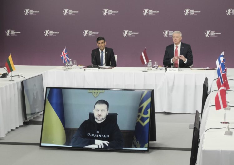 El presidente de Ucrania, Volodimir Zelenski (en la pantalla), se dirige a los participantes en la Cumbre de la Fuerza Expedicionaria Conjunta (JEF), ante la mirada del primer ministro británico, Rishi Sunak (izq.), y del primer ministro letón, Krisjanis Karins, en Riga, Letonia, este 19 de diciembre. EFE/EPA/VALDA KALNINA