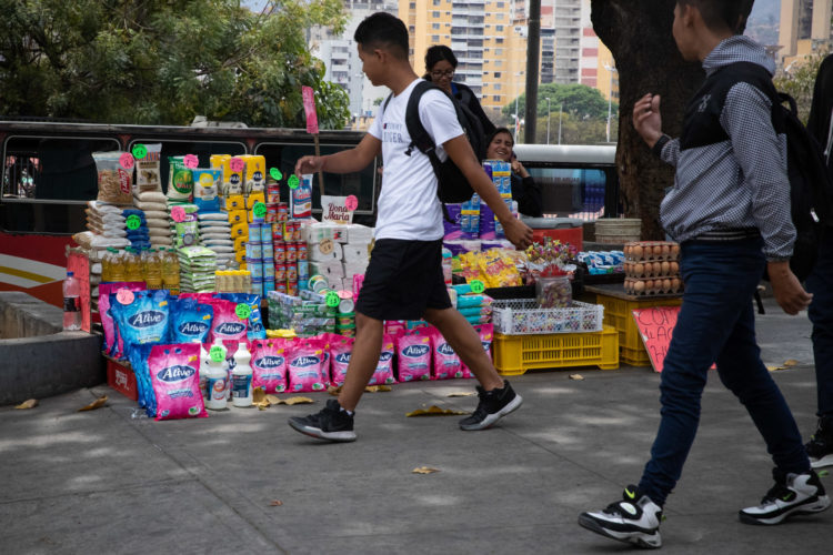 Personas caminan frente a puesto informal de comida y productos básicos en Caracas (Venezuela). EFE/ Rayner Peña R