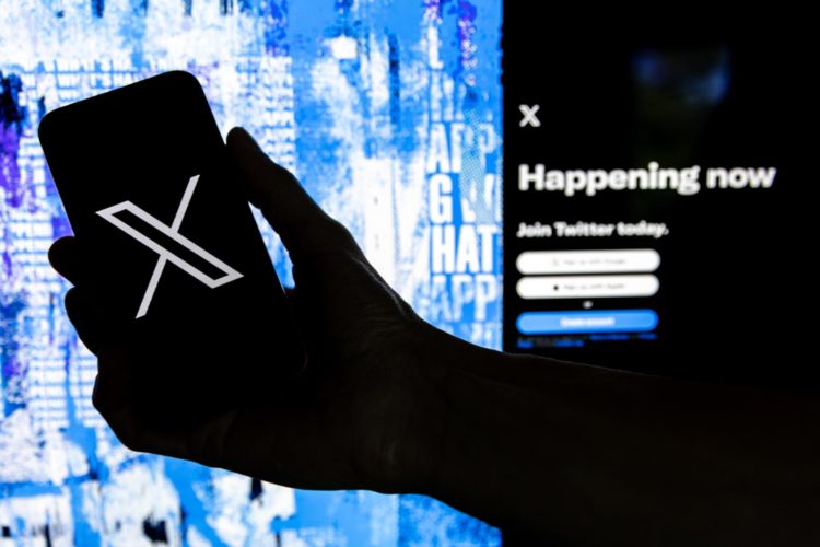 Fotografía que muestra un usuario mientras sostiene un teléfono móvil que muestra el logotipo 'X' frente a la página principal de Twitter. EFE/EPA/Etienne Laurent