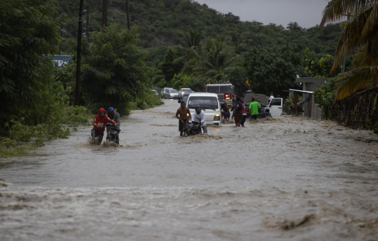 Personas cruzan con dificultad la carretera que se encuentra inundada producto de las intensas lluvias, hoy en San José de Ocoa (República Dominicana). EFE/Orlando Barría