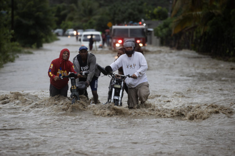 Personas cruzan con dificultad la carretera que se encuentra inundada producto de las intensas lluvias, ayer en San José de Ocoa (República Dominicana). EFE/Orlando Barría