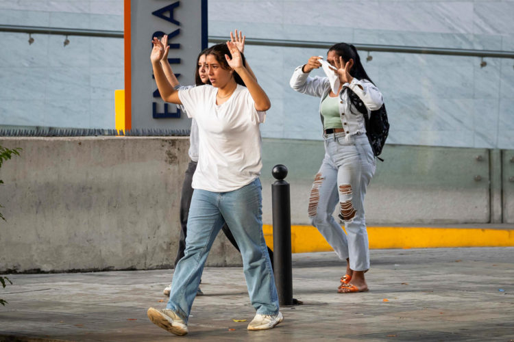 Tres jóvenes avanzan con las manos arriba para evitar ataque de integrantes de la Policía Nacional Bolivariana (PNB) y la Guardia Nacional Bolivariana (GNB) durante enfrentamientos con manifestantes opositores el lunes, durante una protesta contra de los resultados de las elecciones presidenciales en Caracas (Venezuela). EFE/ Ronald Peña R.
