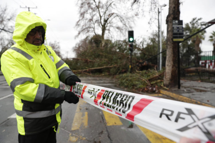Personal de seguridad resguarda las calles afectadas por un árbol caído, producto del fuerte viento y las lluvias durante la madrugada, este viernes en Santiago (Chile). EFE/ Elvis González