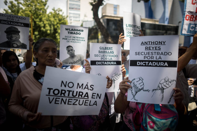 Fotografía de archivo de personas con carteles que muestran imágenes de detenidos durante una manifestación frente a la sede del Ministerio de Servicio Penitenciario, en Caracas. EFE/ Miguel Gutierrez