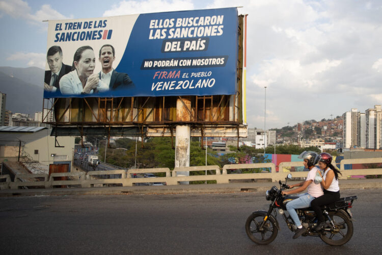 Fotografía del 28 de febrero de 2025 de personas en motocicleta transitando frente a un cartel de la oposición venezolana en Caracas (Venezuela). EFE/ Ronald Peña R