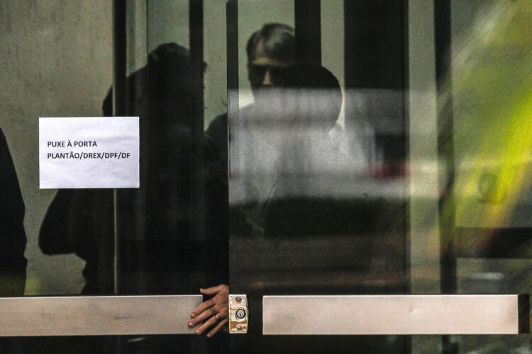Fotografía que muestra al expresidente de Brasil Jair Bolsonaro (c) detrás de una puerta de vidrio este domingo, en la Superintendencia de la Policía Federal en Brasilia (Brasil). EFE/ Isaac Fontana