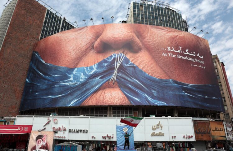 Un iraní sostiene la bandera nacional de Irán frente a una enorme valla publicitaria antiestadounidense que hace referencia al presidente de EE. UU. Donald Trump y al estrecho de Ormuz, este sábado 2 de mayo en la plaza Valiasr de Teherán, Irán. EFE/EPA/ABEDIN TAHERKENAREH