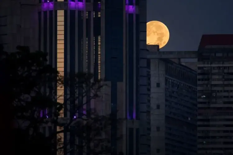 CARACAS (VENEZUELA), 14/03/2025.- Vista de la luna llena junto a una de las torres de Parque Central este viernes, después del eclipse lunar total conocido como "luna roja", en Caracas (Venezuela). EFE/ Miguel Gutiérrez